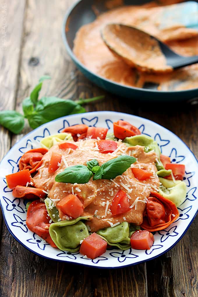 tuscan tomato basil tortellini on a plate with sauce and a serving spoon in a skillet faded in the background.