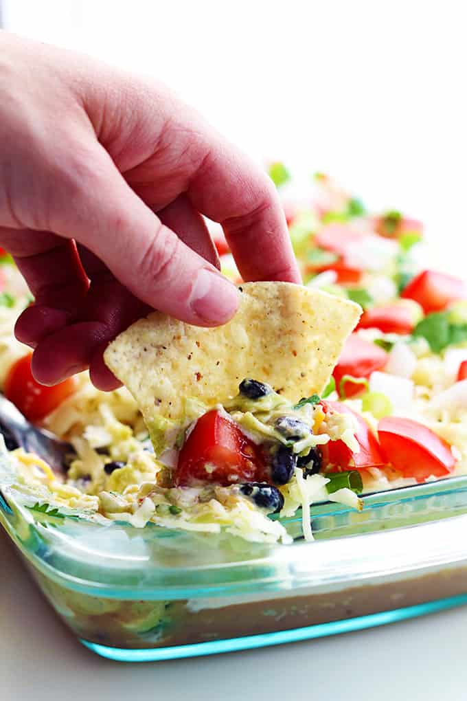a hand scooping some 9 layer dip from a tray with a chip.