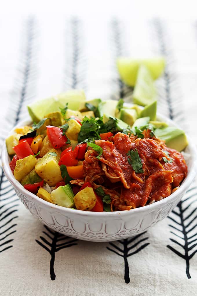 slow cooker adobo chicken with veggies and a slice of lime on top of rice in a bowl with slices of lime faded in the background.