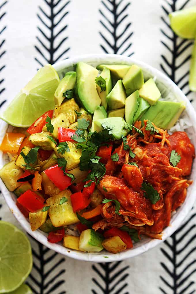 top view of slow cooker adobo chicken with veggies and a slice of lime on top of rice in a bowl with slices of limes on the side.