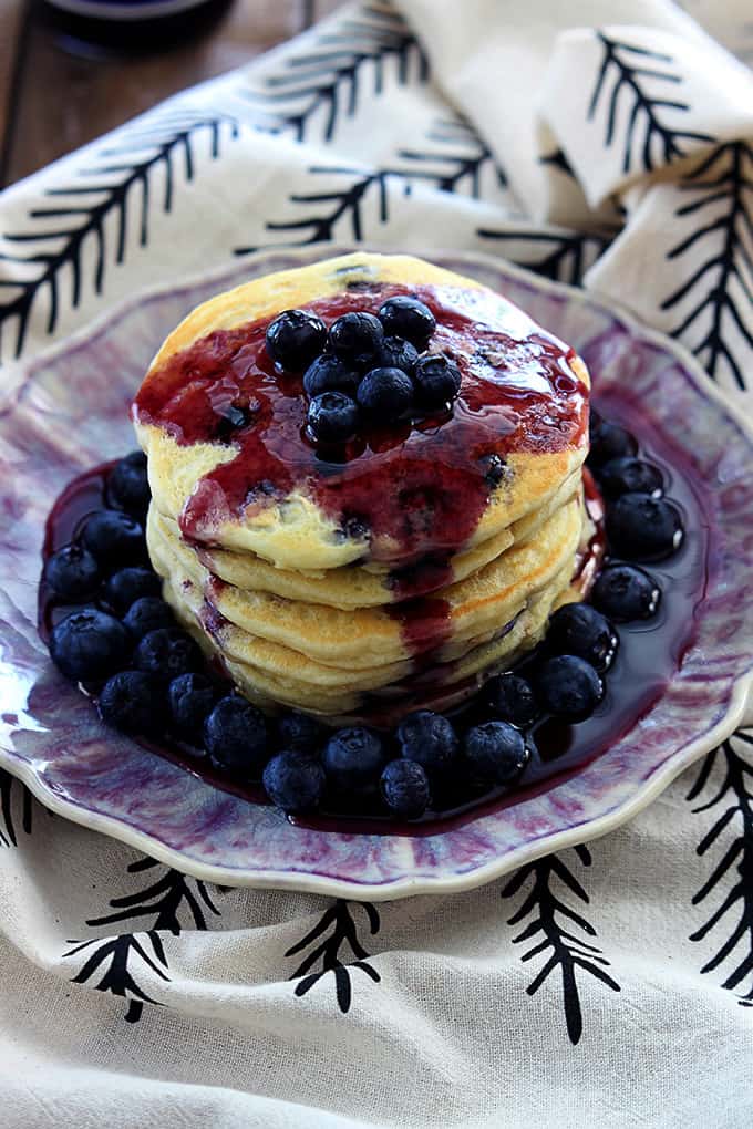 a stack of blueberry oatmeal pancakes with blueberries and blueberry syrup on top on a plate.