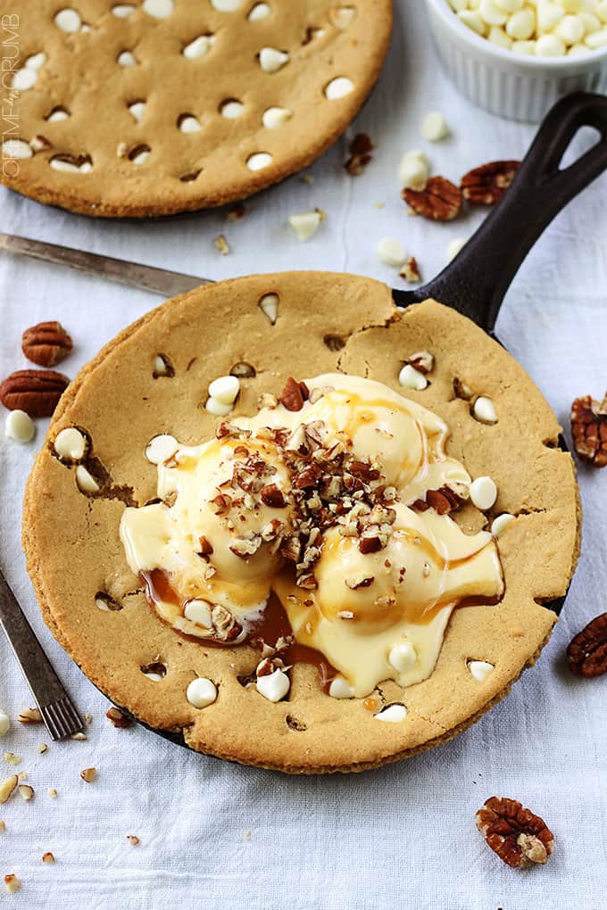 top view browned butter skillet blondie in a skillet topped with ice cream and nuts surrounded by nuts, white chocolate chips and another blondie in a skillet.