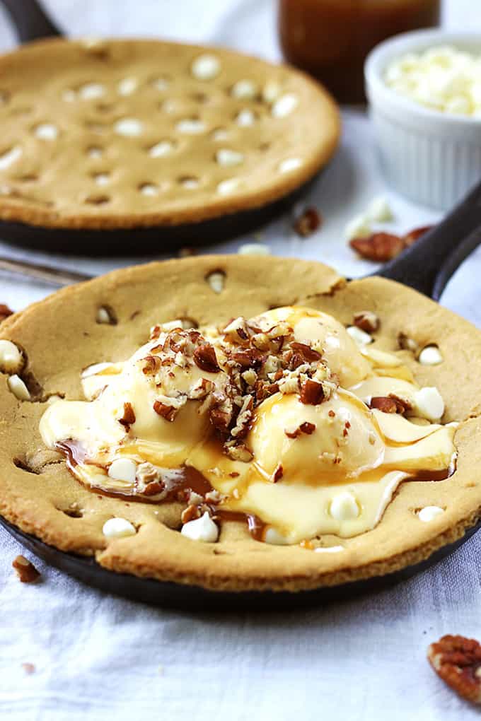 browned butter skillet blondie in a skillet topped with ice cream and nuts with another blondie in a skillet in the background.