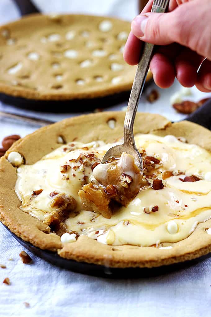 a hand scooping some ice cream and a browned butter skillet blondie with another blondie in a skillet in the background.