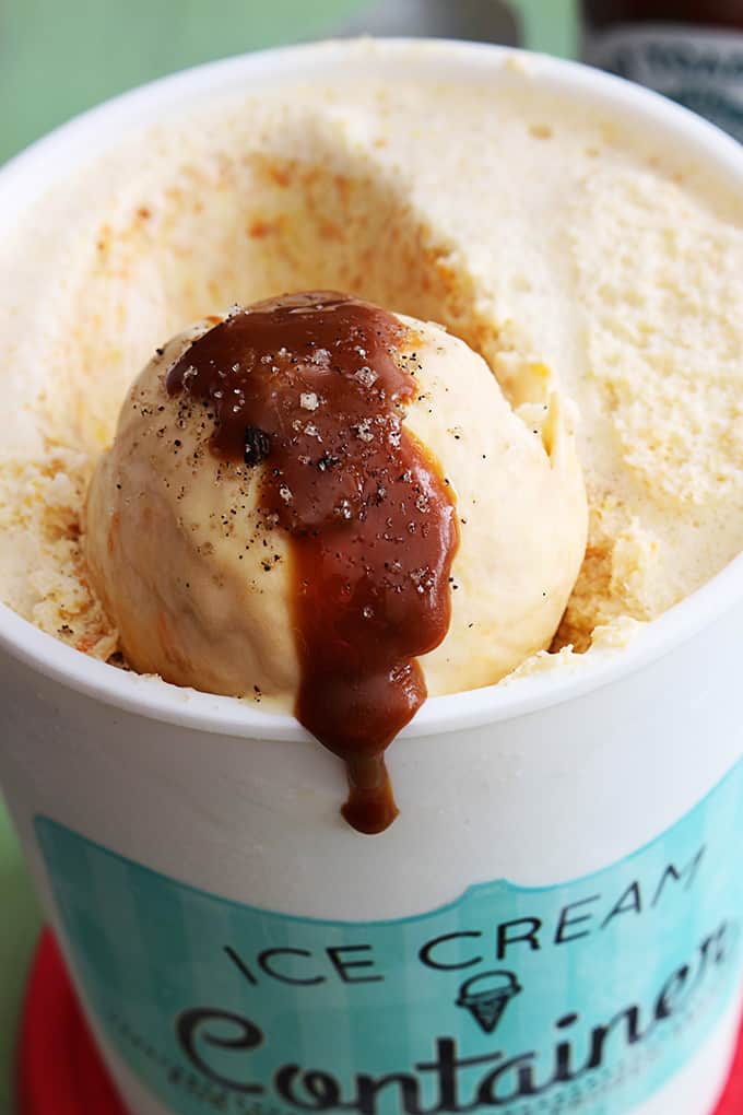 butterscotch ice cream in an ice cream container with sauce on a scoop of ice cream.
