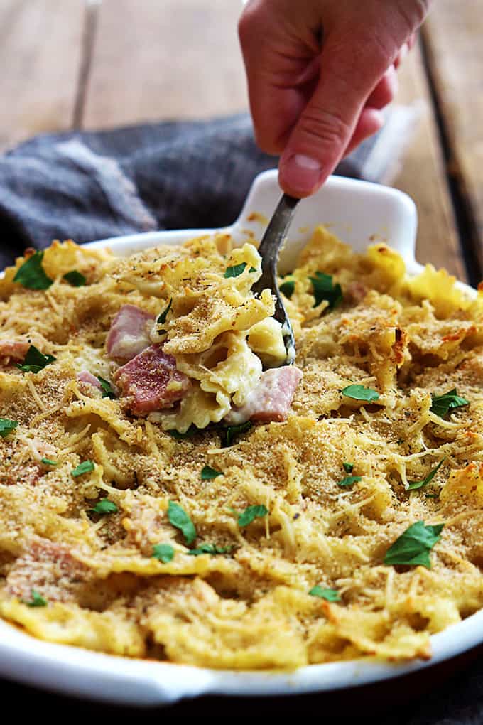 a hand scooping chicken cordon bleu pasta bake from a serving tray.