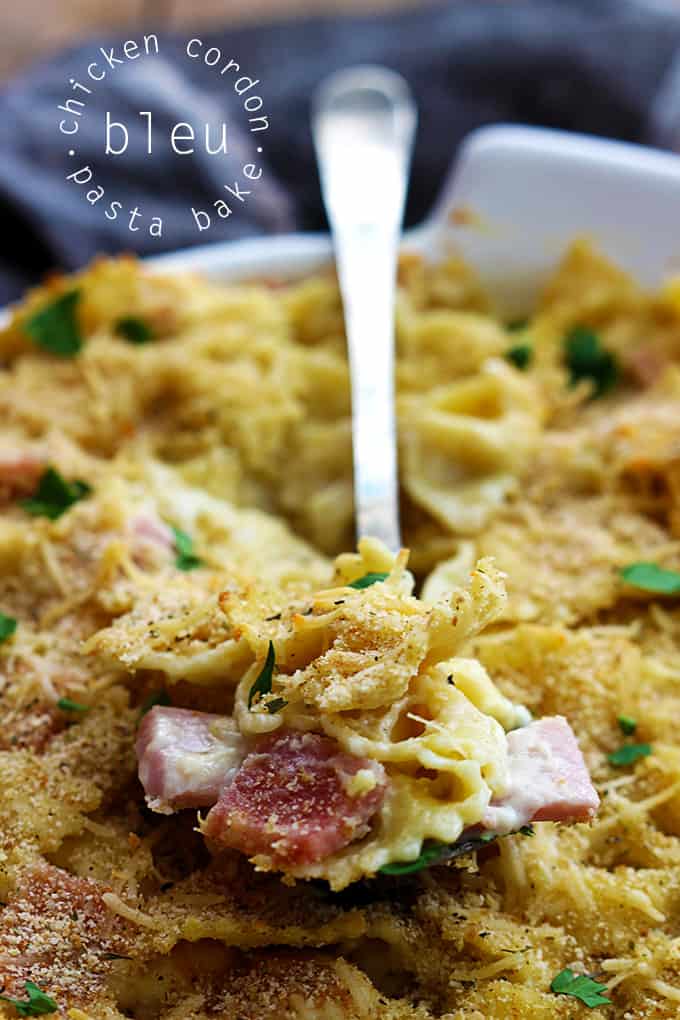 a tray of chicken cordon bleu pasta bake with a serving spoon with a scoop of pasta on top and the title of the recipe written on the top left corner of the image.