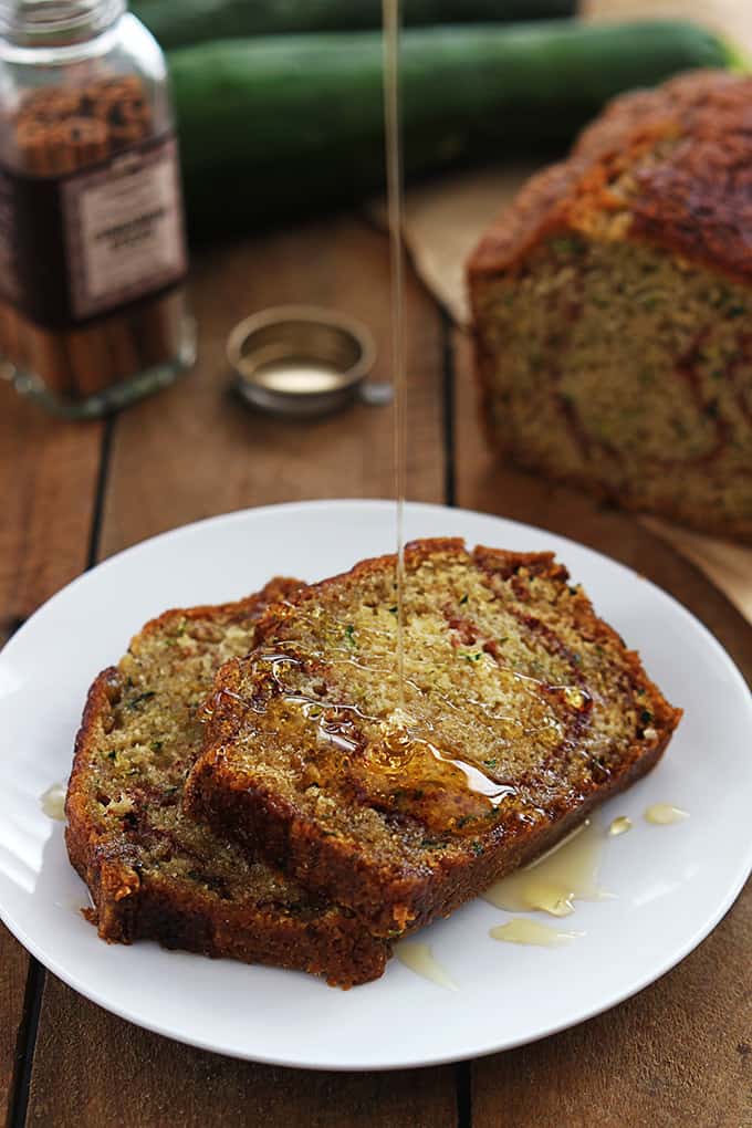 slices of cinnamon swirl zucchini bread on a plate with honey being poured on top.