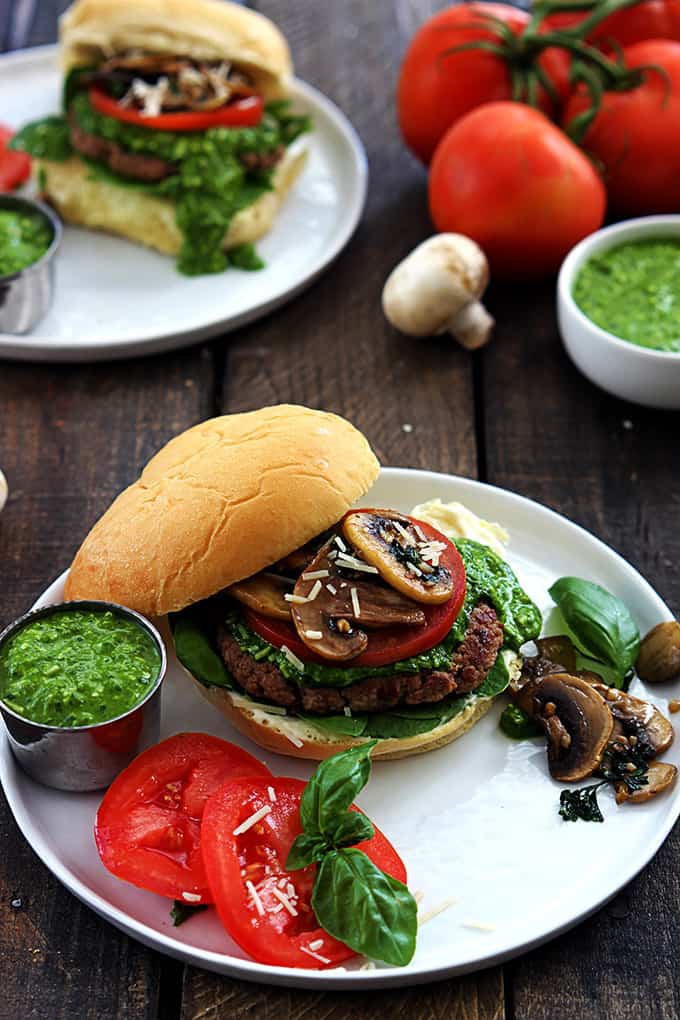 a garlic pesto turkey burger with toppings on a plate with another burger on a plate and more toppings in the background. 