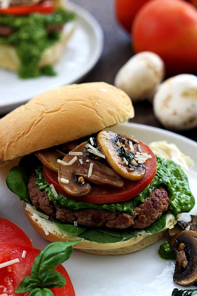 a garlic pesto turkey burger on a plate surrounded by toppings.
