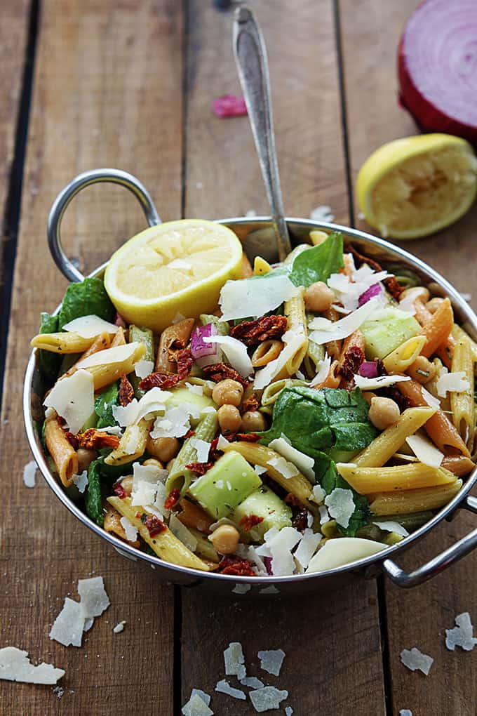 Greek pasta salad in a metal bowl with half of a lemon and red onion on the side.