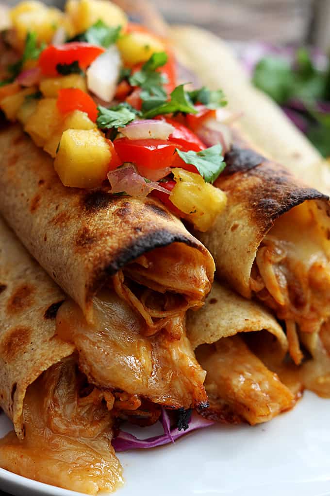 close up of slow cooker Hawaiian bbq chicken taquitos topped with pineapple salsa on a plate.