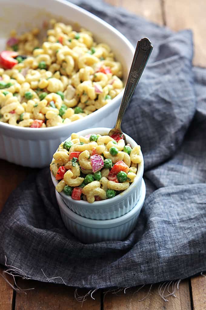 top view of honey dijon macaroni salad and a fork in a small bowl on top of another bowl with more macaroni salad in a dish in the background.