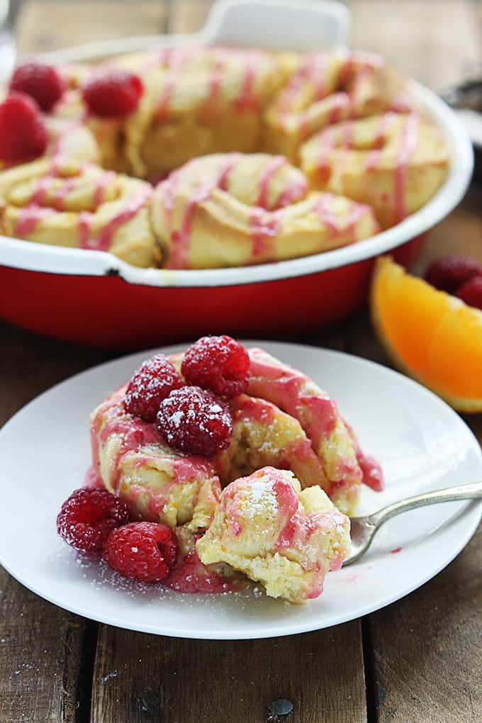 a orange raspberry sweet roll on a plate with a bite on a fork and more rolls in the background.
