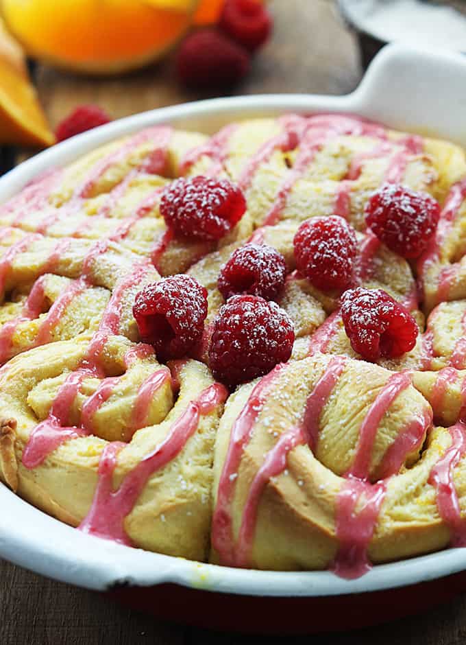 orange raspberry sweet rolls in a serving tray topped with icing and raspberries.