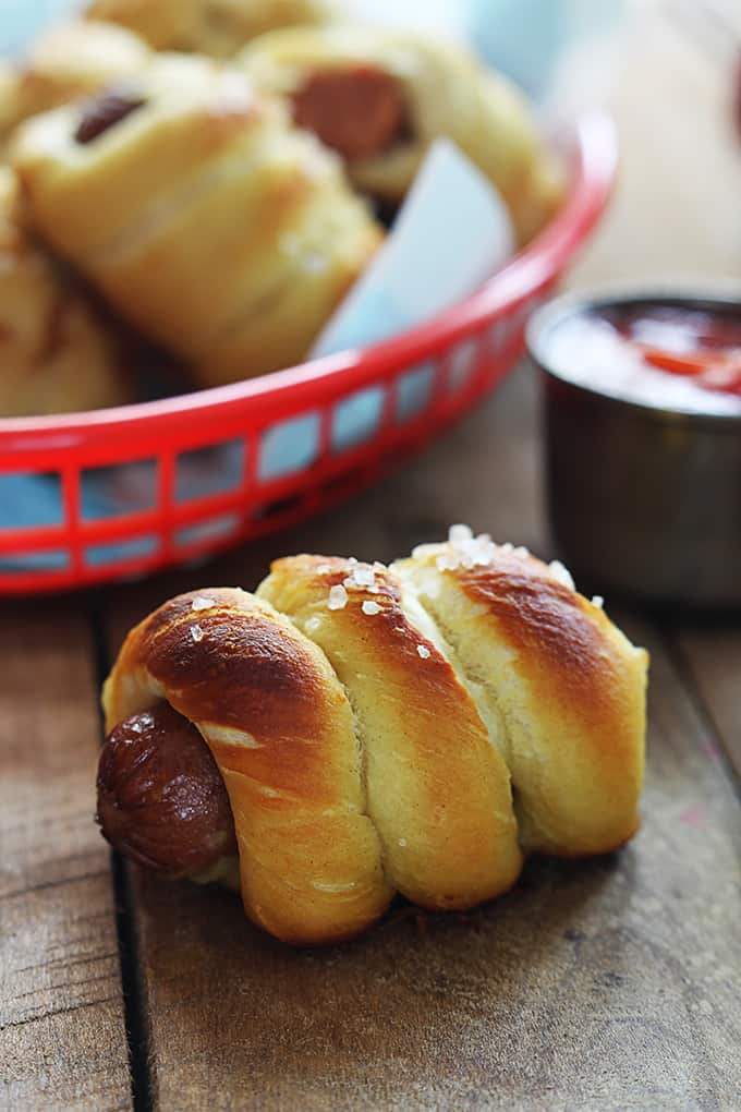 a pretzel dog on a table with more pretzel dogs in a basket.