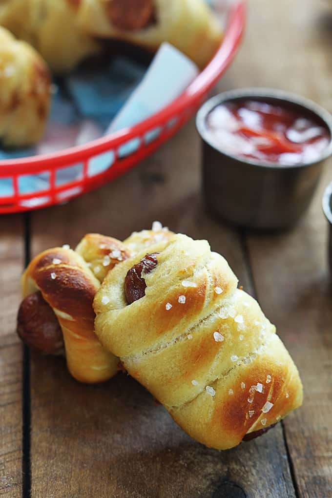 stacked pretzel dogs on a table with more in a basket faded in the background.