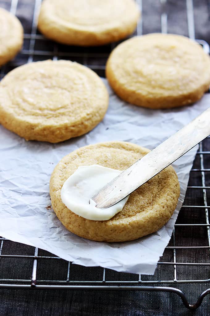 pumpkin sugar cookies on a cooling rack with a knife spreading cream cheese frosting on top of the first cookie.