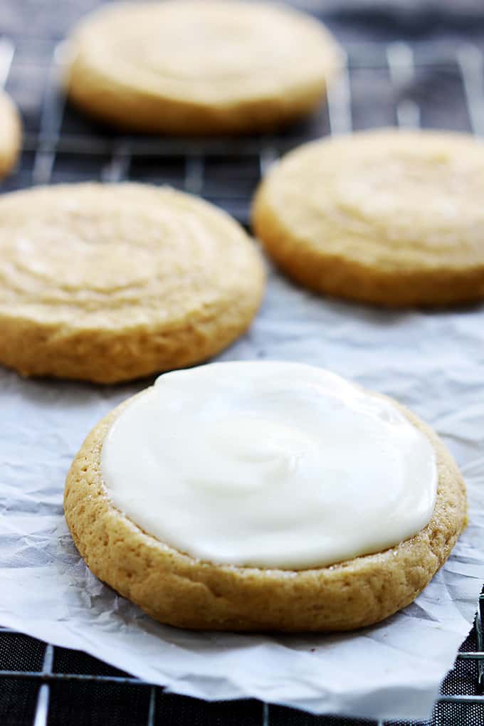 pumpkin sugar cookies on a cooling rack with the first cookie having cream cheese frosting on top.