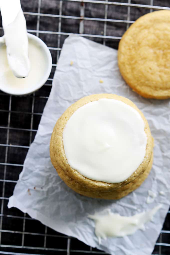 top view of stacked pumpkin sugar cookies with the top one frosted and a dipping bowl of cream cheese frosting with a knife on top and another cookie on the side.