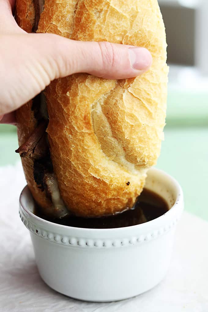 a hand dipping a slow cooker French dip sandwich in a bowl of French dip.