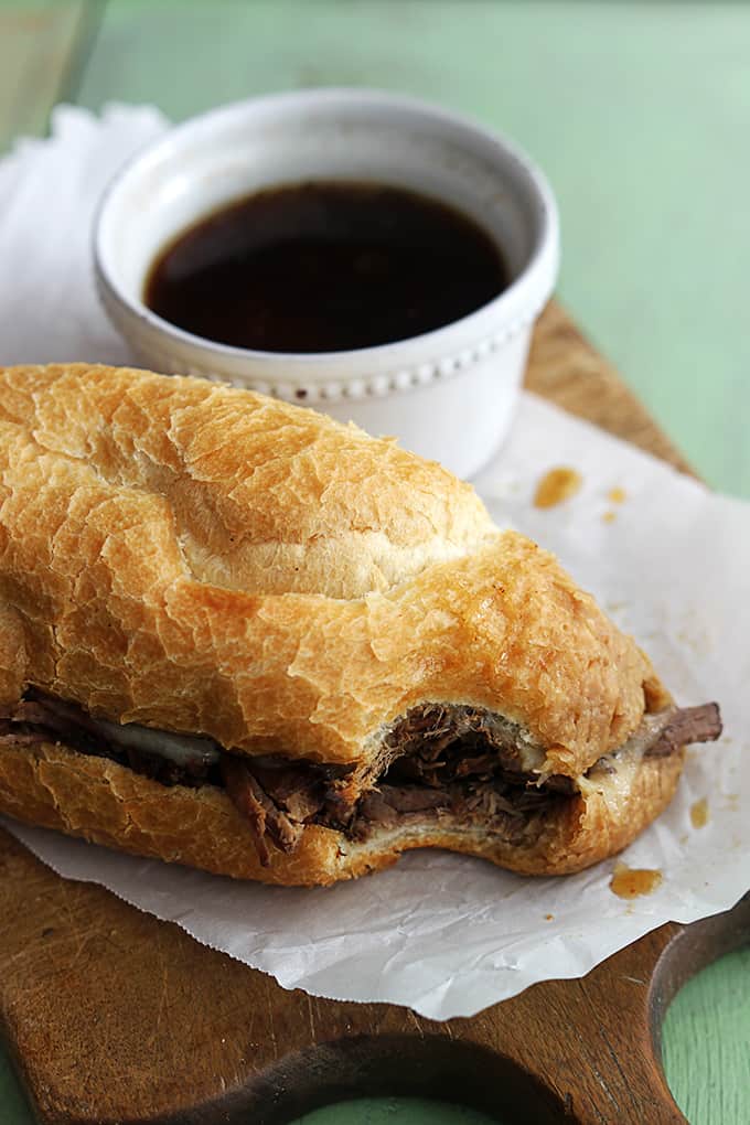 a slow cooker French dip sandwich with a bite taken out of it next to a bowl of French dip.
