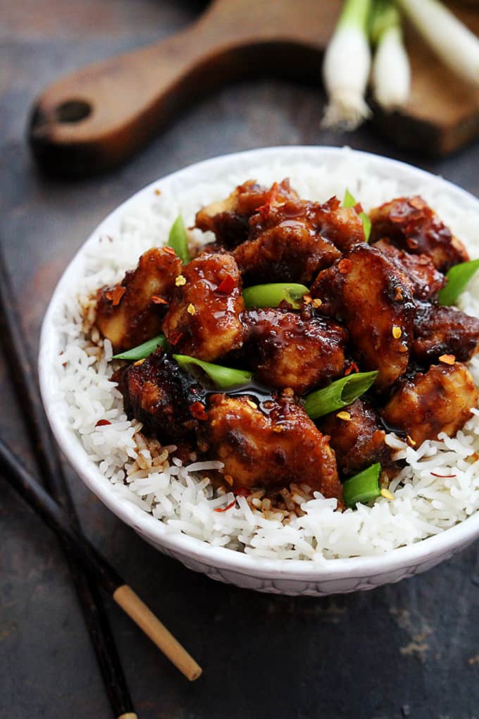 general tso's chicken on rice in a bowl with chopsticks on the side.