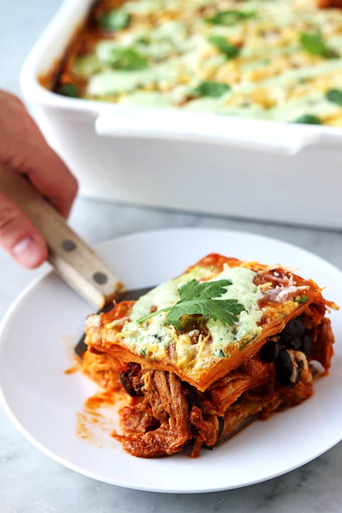 a hand holding a spatula with a serving of enchilada casserole on top with a plate underneath.