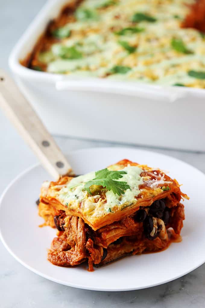 enchilada casserole on a spatula on a plate with a serving tray of enchilada casserole in the background.