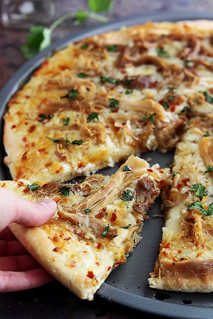 a hand taking a slice of Thai sweet chili pork pizza.