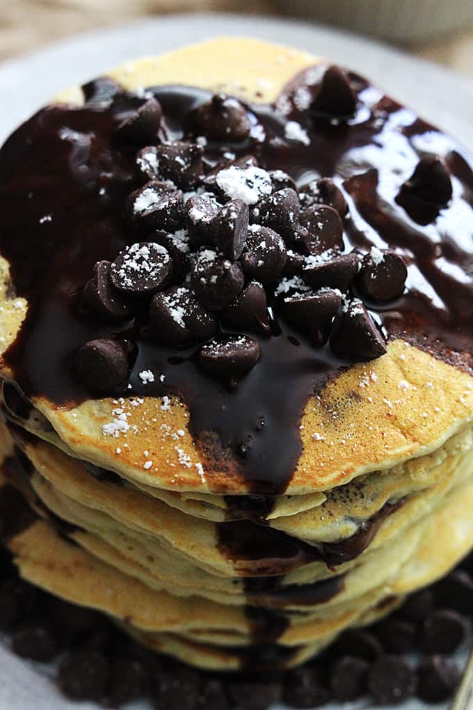 top view of a stack of zucchini chocolate chip pancakes on a plate topped with chocolate chips and chocolate syrup.