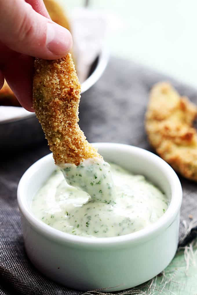 a hand dipping a baked avocado fry in sauce.