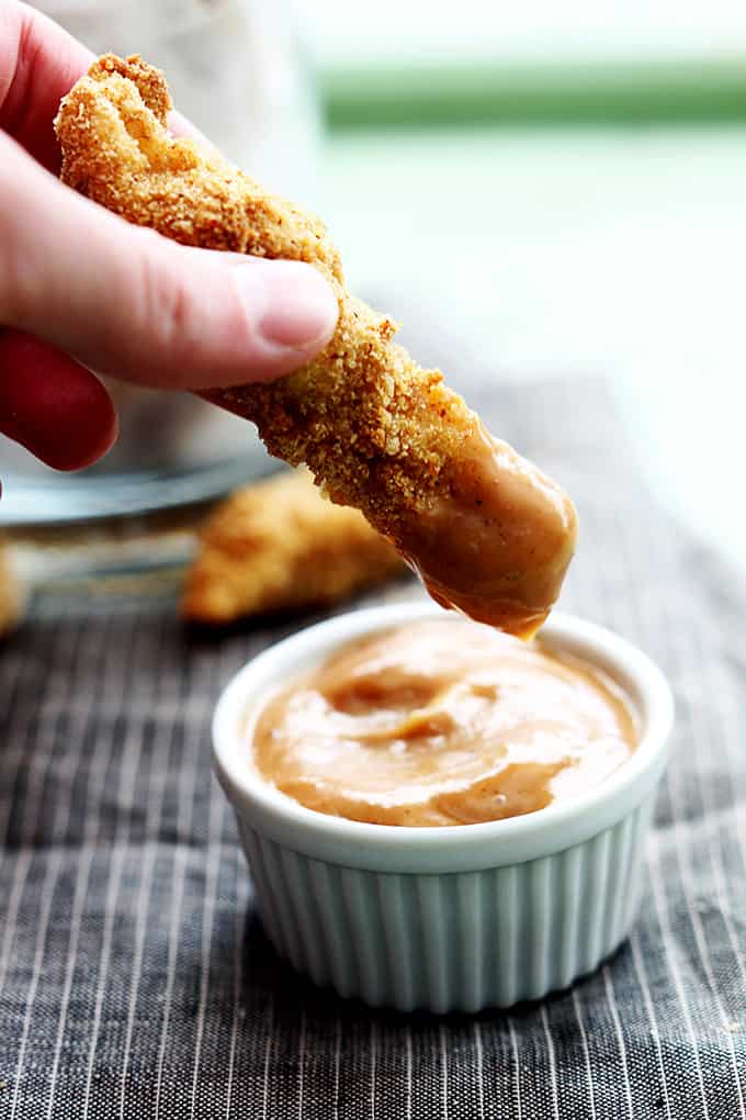 a hand holding a chicken fry just dipped in fry sauce above a small dipping bowl of fry sauce.