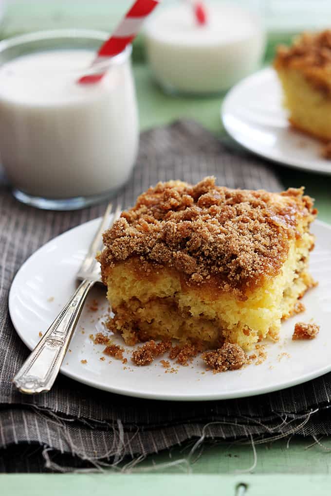 a slice of cake mix sour cream coffee cake with a fork on a plate with glasses of milk and another piece of cake on a plate faded in the background.