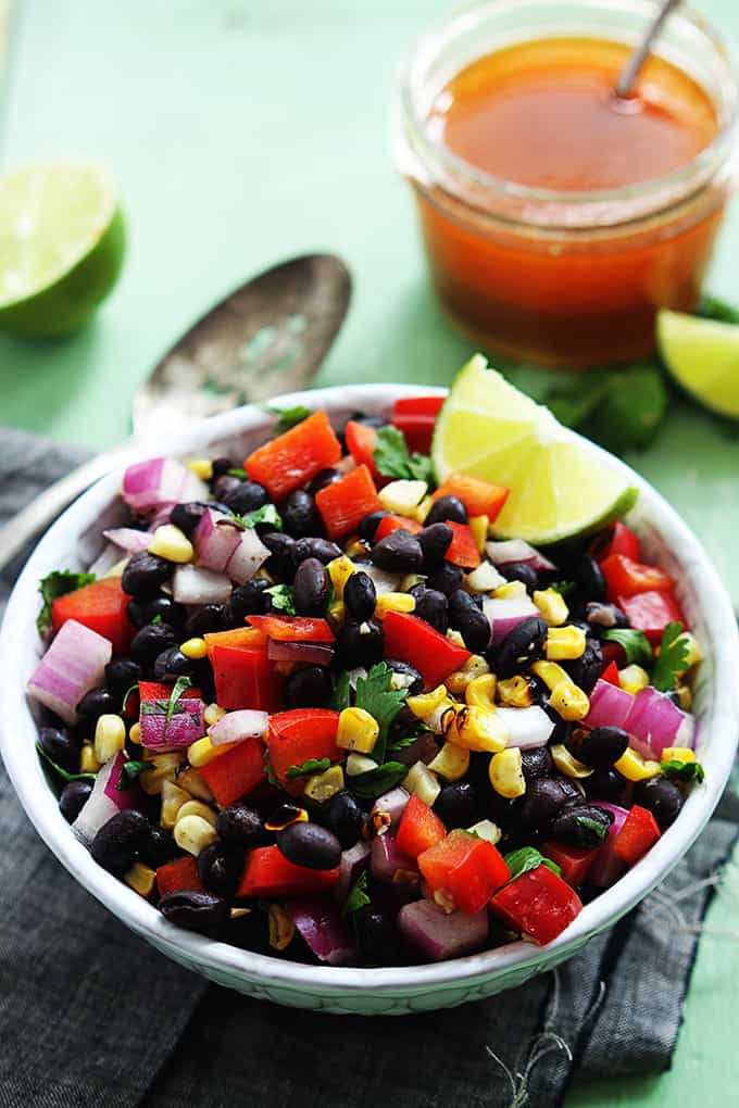 honey chipotle black bean salad with a slice of lime in a bowl with slices of lime, a spoon and jar of honey in the background.