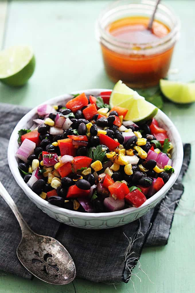 honey chipotle black bean salad with a slice of lime in a bowl with a spoon, slices of lime and a jar of honey on the side.
