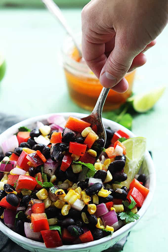 a hand taking a scoop of honey chipotle black bean salad from a bowl.