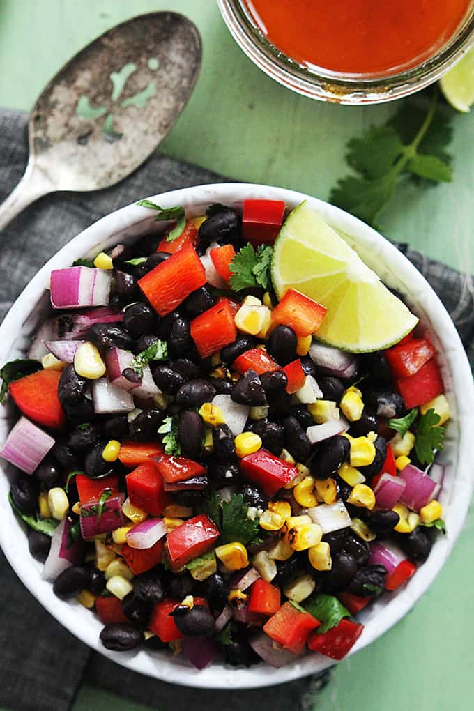 top view of honey chipotle black bean salad with a slice of lime in a bowl with a spoon and jar of honey on the side.