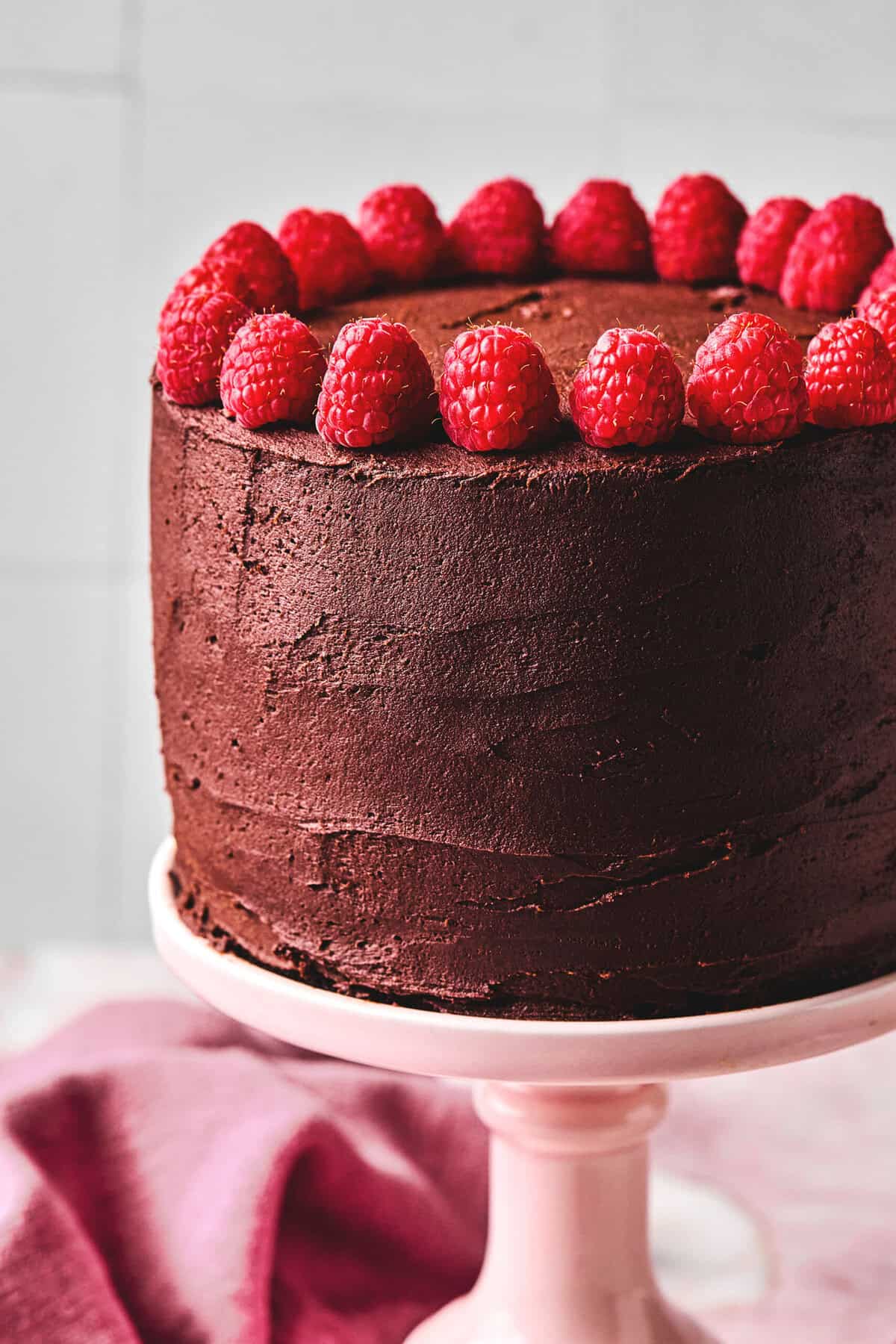 raspberries topping a chocolate frosted cake on a cake stand.