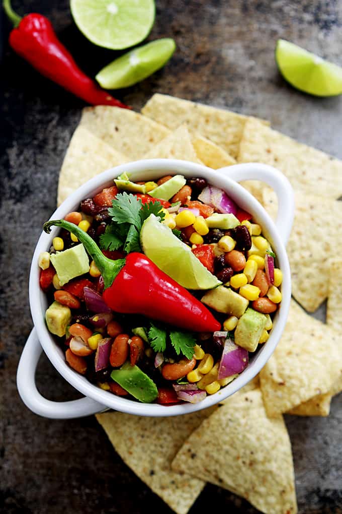 top view of cowboy caviar in a bowl topped with a red chili pepper and a slice of lime with chips, more peppers and lime slices on the side.