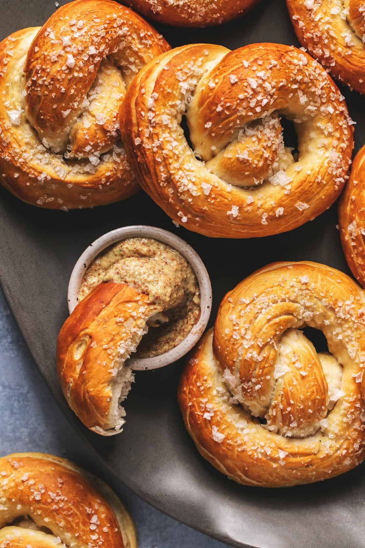 Piece of German soft pretzel dipping into mustard sauce on platter.