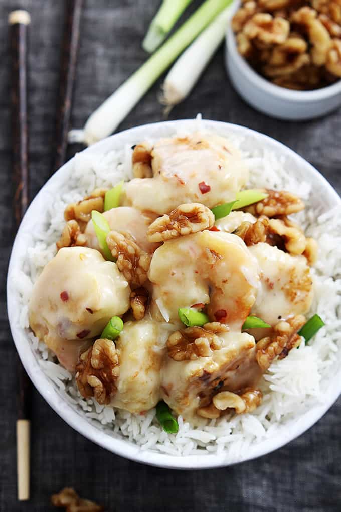 top view of honey walnut shrimp on rice in a bowl with chopsticks on the side and green onions and a small bowl of walnuts in the background.