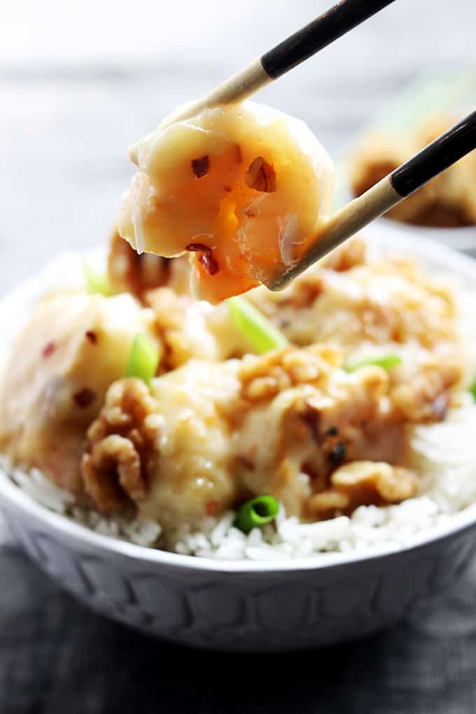 chopsticks holding a honey walnut shrimp with a bowl of honey walnut shrimp on rice faded in the background.