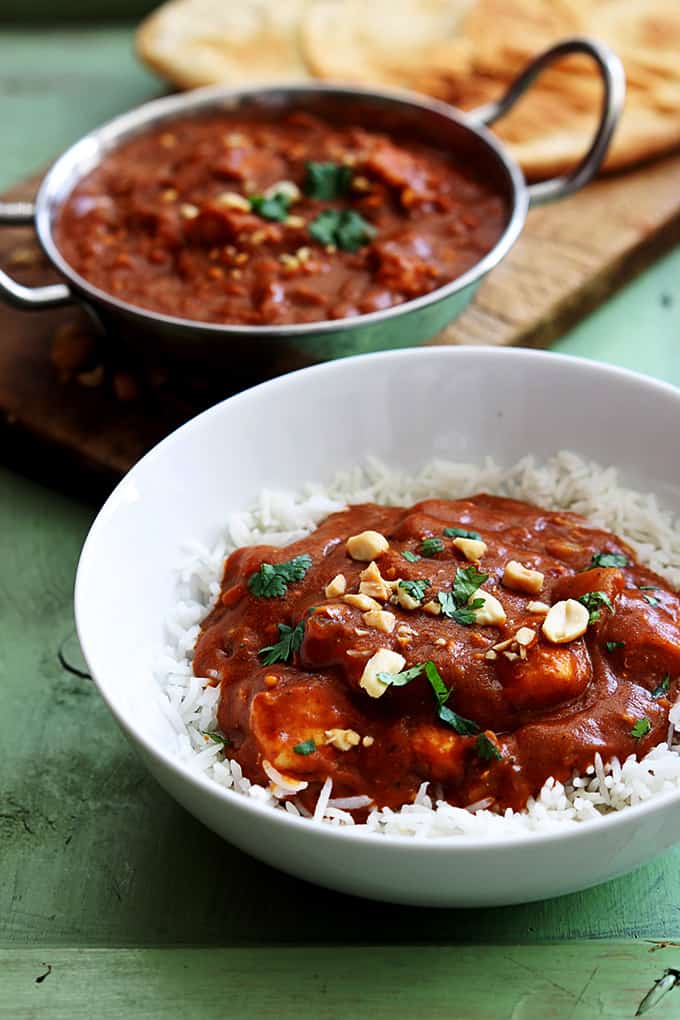 Indian butter chicken on rice in a bowl with butter chicken in a cooking pan in the background.