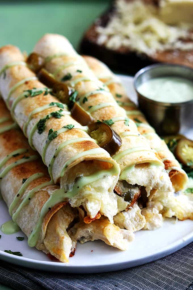 slow cooker jalapeño popper chicken taquitos on a plate with sauce on the side.