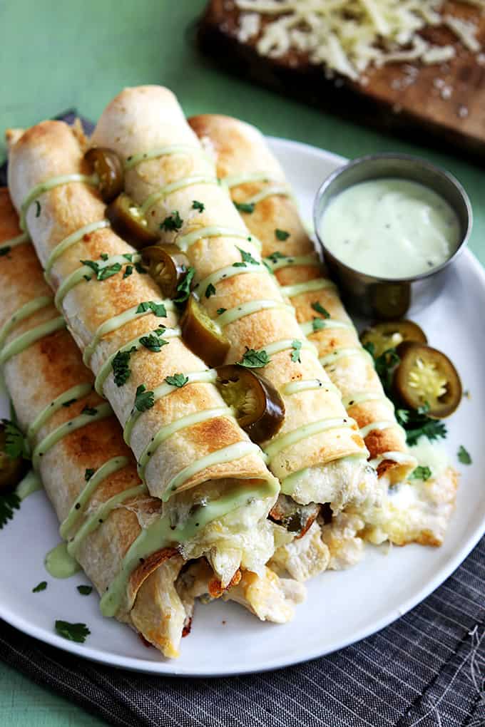 top view of slow cooker jalapeño popper chicken taquitos on a plate with sauce on the side.