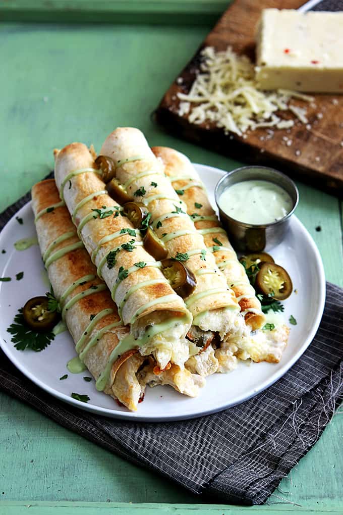 slow cooker jalapeño popper chicken taquitos on a plate with a block of cheese on a wooden cutting board in the background.