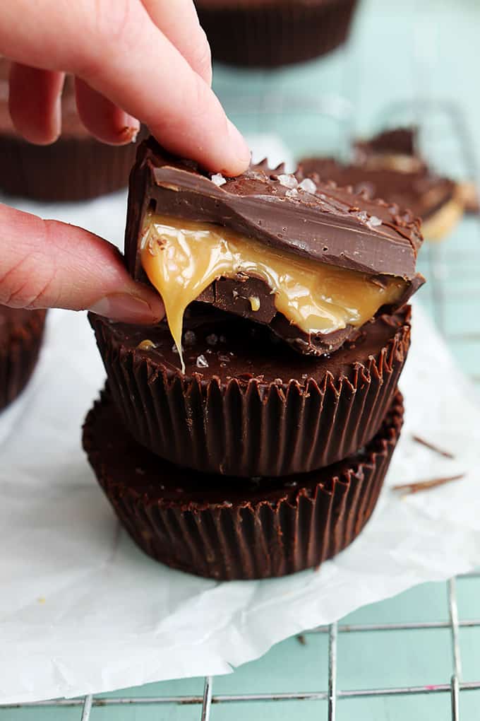 stacked salted caramel cups on a cooling rack with half of a caramel cup on top being taken by a hand.