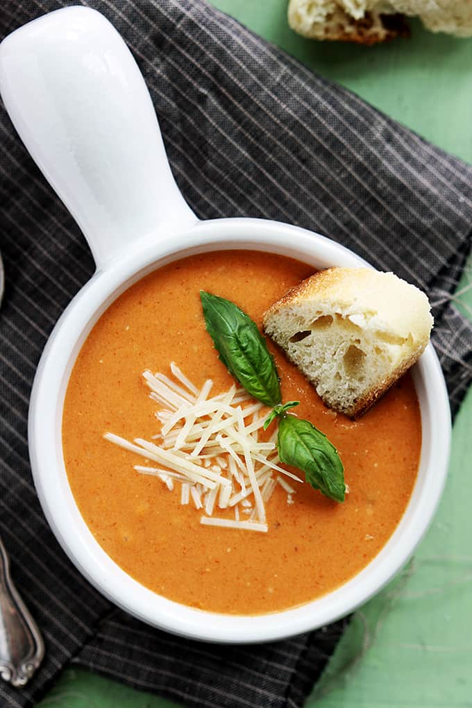 top view of slow cooker tomato basil parmesan soup in a bowl with a piece of bread dipped in it.