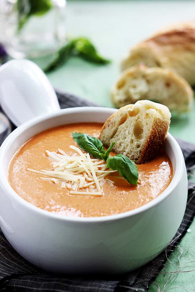 slow cooker tomato basil parmesan soup in a bowl with a piece of bread dipped in it.